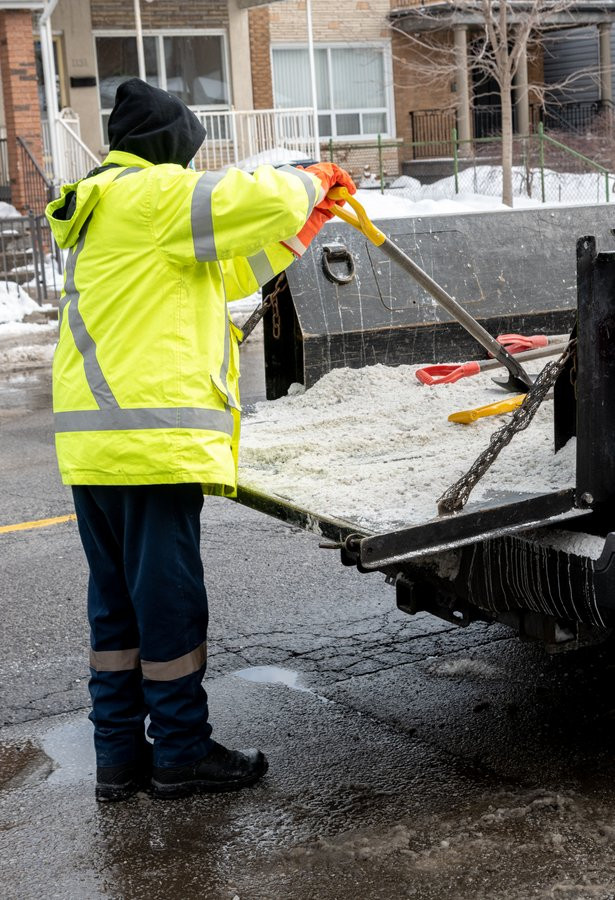 A City of Toronto employee is working on salting the roads with a shovel.